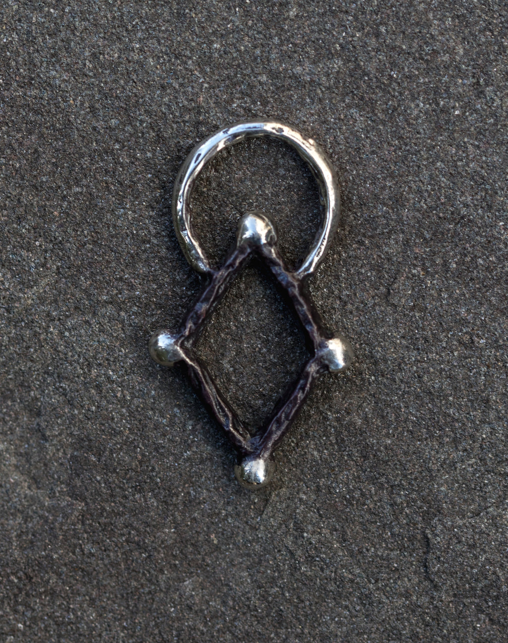 Silver geometric pendant on a dark textured surface