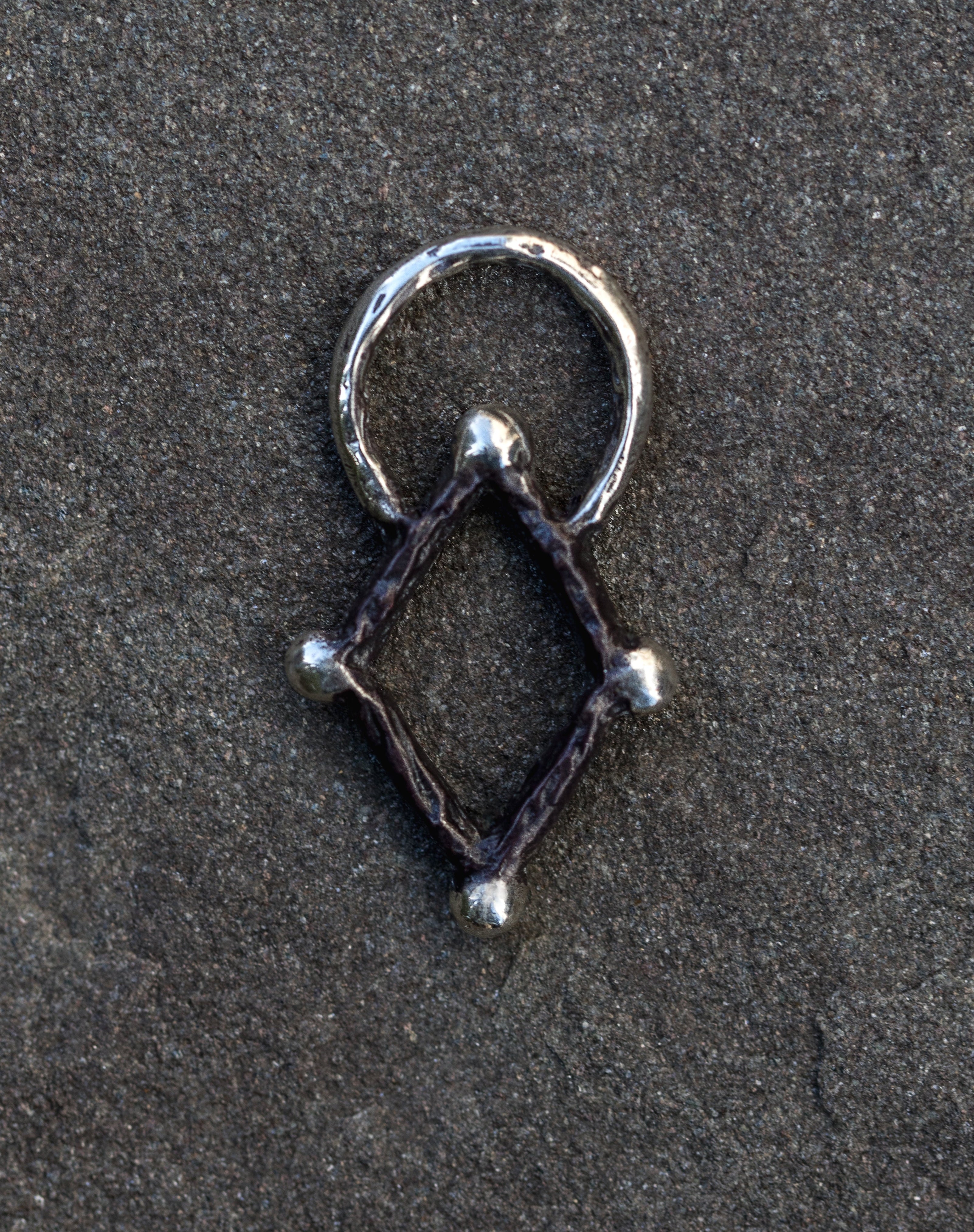 Silver geometric pendant on a dark textured surface